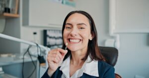 smiling young woman holding a dental veneer